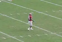 American football player waiting to field a punt on a green field.